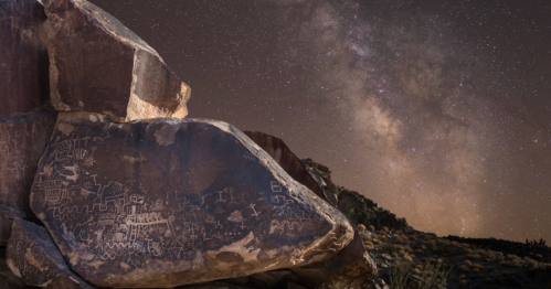 Petroglyphs on a rock under a starry night sky, showcasing the Milky Way in the background.