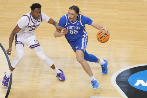A basketball player in a blue jersey dribbles the ball while being closely guarded by an opponent in a white jersey.