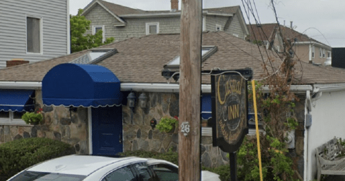 A stone building with a blue awning and a sign reading "Café Inn," surrounded by greenery and parked cars.