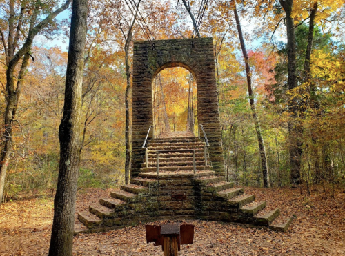 Stone archway with stairs surrounded by colorful autumn trees and fallen leaves.