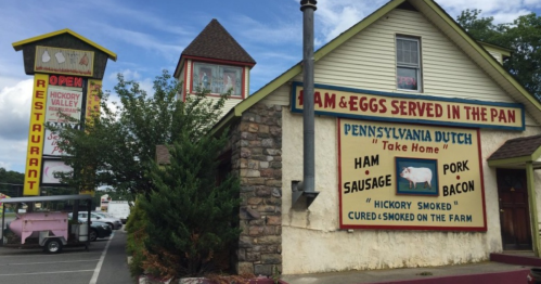 A colorful restaurant exterior featuring a sign for ham and eggs, with a Pennsylvania Dutch theme and a nearby signpost.