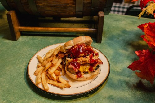 A hearty burger topped with bacon, cheese, and ketchup, served with a side of golden fries on a plate.