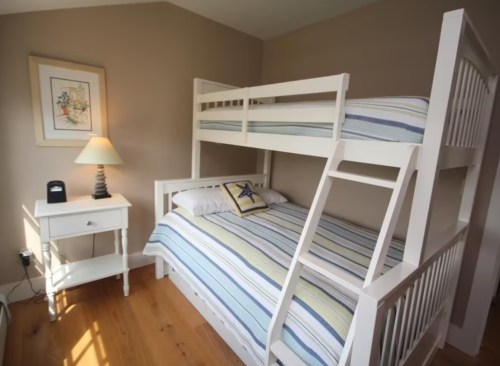 A cozy bedroom featuring a bunk bed, a double bed, a nightstand, and a lamp against a neutral wall.