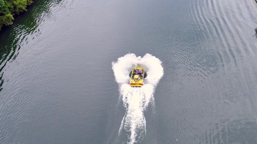 Aerial view of a speedboat creating a splash on a calm river, surrounded by greenery.