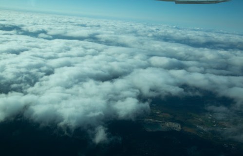 Aerial view of fluffy white clouds covering a green landscape under a clear blue sky.