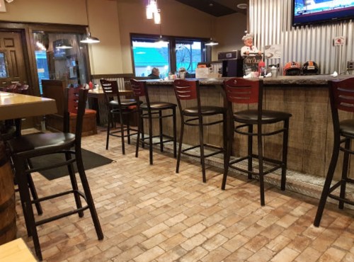 Interior of a restaurant featuring a bar with high stools, wooden accents, and a tiled floor.