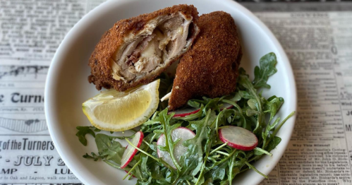 A plate with a crispy fried chicken dish, a lemon wedge, and a fresh arugula salad with radish slices.