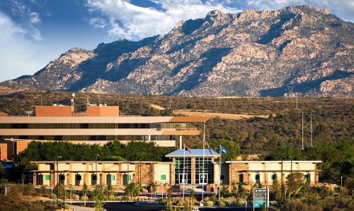A modern building in the foreground with mountains in the background under a clear blue sky.