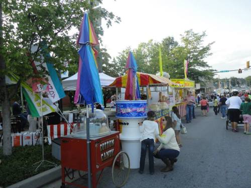 A lively street fair scene with food stalls, colorful umbrellas, and people enjoying the festivities.