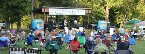 A crowd enjoys live music at the International Pottery Festival, seated on lawn chairs under a pavilion.