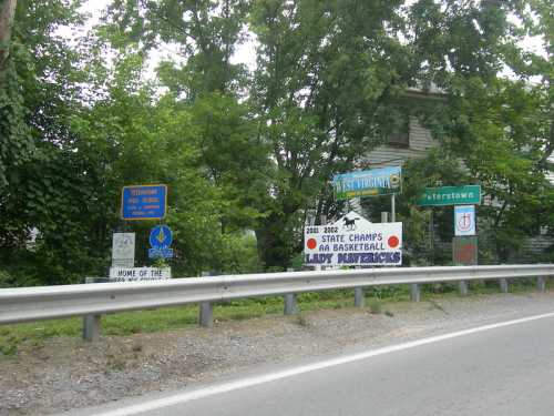 Roadside signs in a green area, featuring school achievements and directional signs for Petersertown, West Virginia.