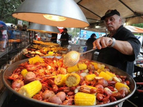 A chef stirs a large pot of seafood, corn, and vegetables at an outdoor cooking event.