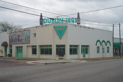 A white building with green accents, featuring a mural and a sign that reads "Dublin 1891," under a cloudy sky.