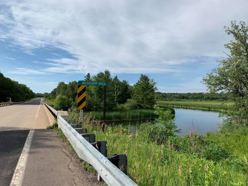 A view of the Mississippi River with a sign, grassy banks, and a clear blue sky in the background.