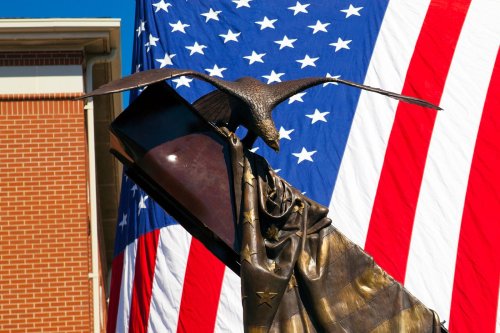 A bronze statue of a figure with an eagle, set against a large American flag backdrop.