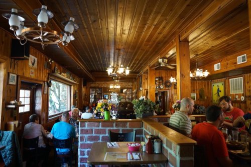 A cozy restaurant interior with wooden walls, tables, and patrons enjoying their meals amidst warm lighting and decor.