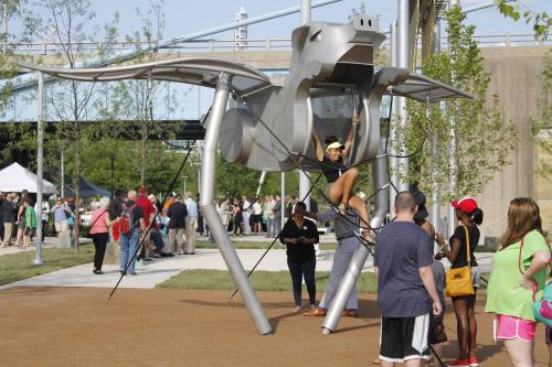 A large metallic sculpture resembling a creature, with people interacting and enjoying a park setting.