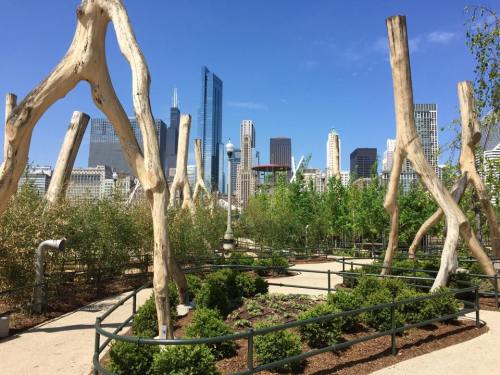 A park with unique wooden structures and greenery, set against a city skyline on a clear blue day.