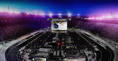 Aerial view of a vibrant NASCAR race at night, with a packed stadium and bright lights illuminating the track.