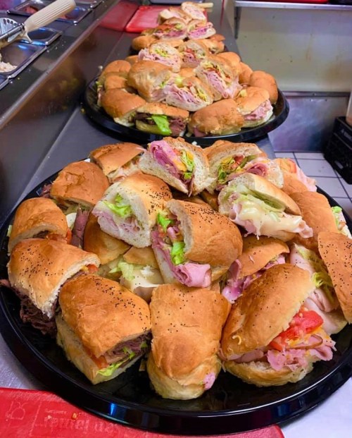 A close-up of two large platters filled with assorted sandwiches, featuring various meats, cheeses, and fresh vegetables.