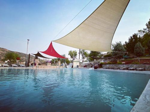 A serene pool area with colorful shade sails, surrounded by trees and mountains under a clear sky.
