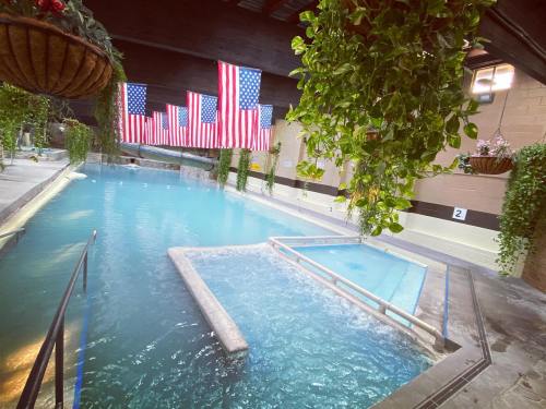 Indoor swimming pool with clear blue water, surrounded by greenery and decorated with American flags in the background.