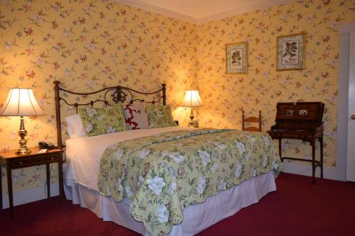Cozy bedroom with a floral wallpaper, a large bed with a green quilt, bedside lamps, and a vintage writing desk.