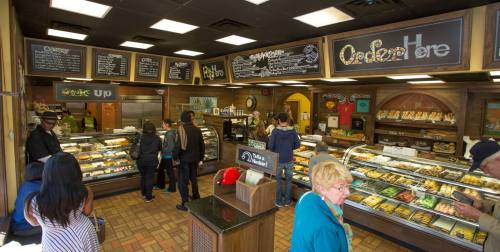 A busy bakery with customers ordering at the counter and a display of various baked goods.