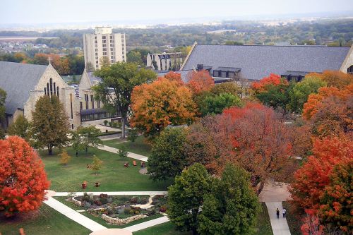 Aerial view of a campus with colorful autumn trees, pathways, and buildings under a clear sky.