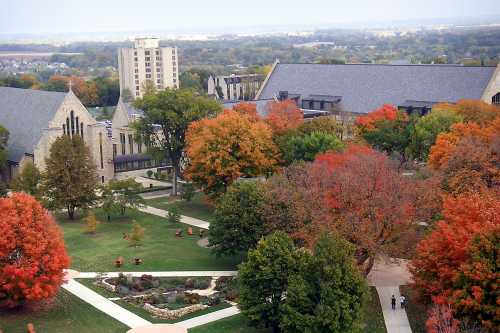 Aerial view of a campus with colorful autumn trees, pathways, and buildings under a clear sky.