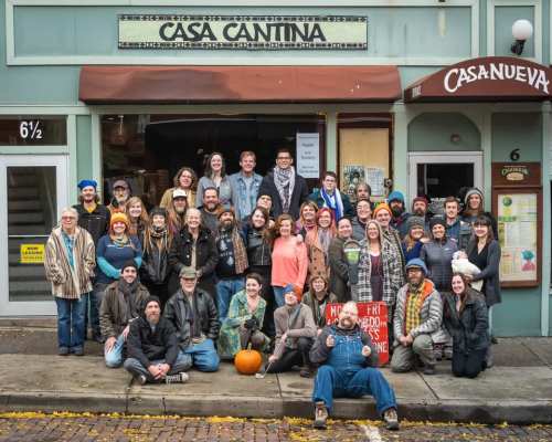 A large group of diverse people poses together outside Casa Cantina, with a pumpkin in front and a festive atmosphere.
