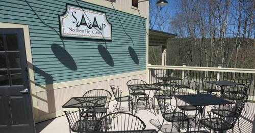 Outdoor dining area with black metal tables and chairs, featuring a sign for "Saap Northern Thai Cuisine."