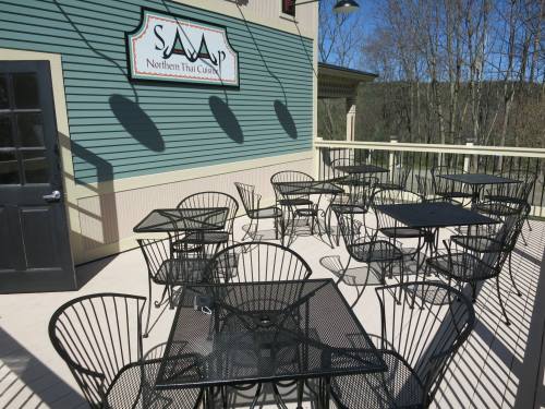 Outdoor dining area with black metal tables and chairs, featuring a sign for "Saaap Northern Thai Cuisine."