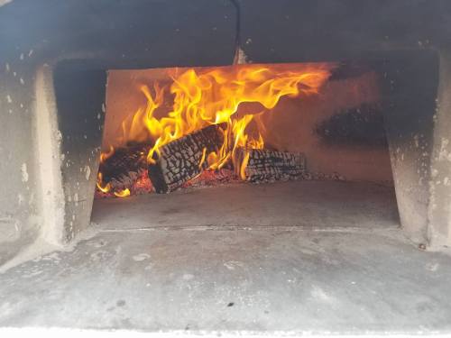 A close-up view of a fire burning inside a stone oven, with flames and glowing embers visible.