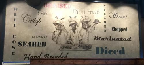 A mural featuring three goat chefs with cooking terms like "braised," "steamed," and "diced" in various fonts.