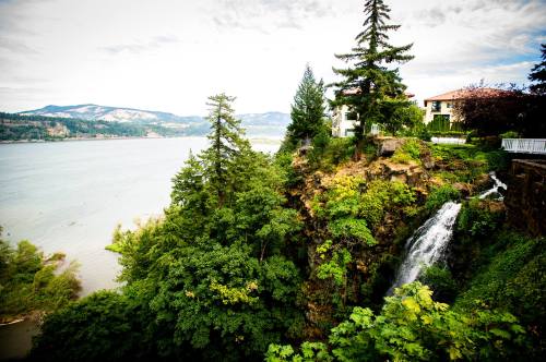 A scenic view of a waterfall cascading down a rocky cliff, surrounded by lush greenery and overlooking a river.