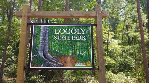 Sign for Logoly State Park featuring a colorful forest scene and a dirt path surrounded by trees.