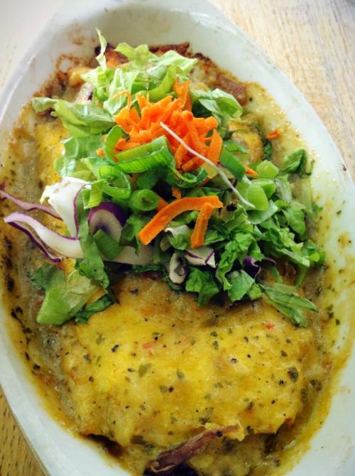 A baked dish topped with melted cheese, fresh greens, and colorful vegetables, served in a white dish.