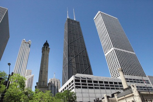 A view of skyscrapers in a city, featuring a tall black building and a historic tower against a clear blue sky.