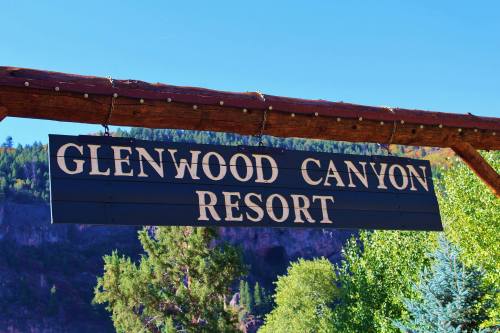 Sign for Glenwood Canyon Resort against a clear blue sky and green trees in the background.