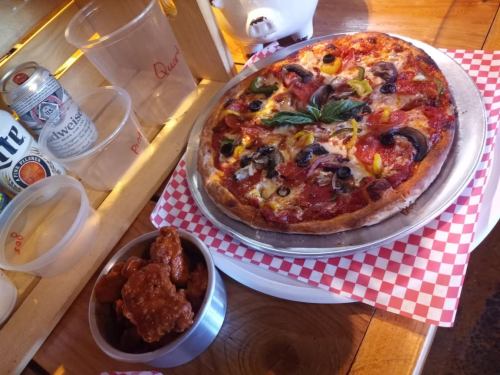 A delicious pizza topped with pepperoni, vegetables, and cheese, served alongside a bowl of spicy chicken wings.