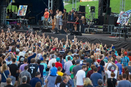 A lively concert scene with a band on stage and a large crowd of fans cheering and enjoying the performance.