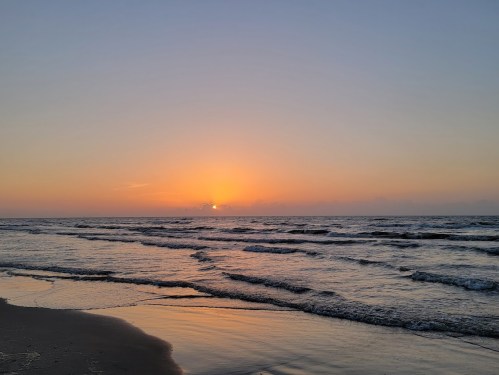 A serene beach at sunset, with gentle waves lapping at the shore and a warm orange glow on the horizon.