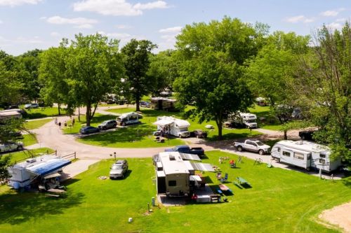 Aerial view of a vibrant campground with RVs, tents, and green trees under a clear blue sky.