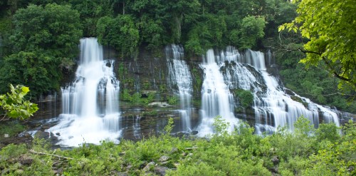 A serene waterfall cascading over rocks, surrounded by lush green trees and foliage.
