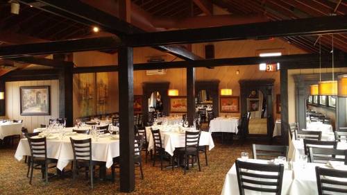 Elegant restaurant interior with tables set for dining, featuring wooden beams and warm lighting.