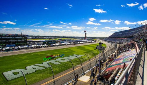 A panoramic view of Daytona International Speedway, bustling with fans under a clear blue sky.