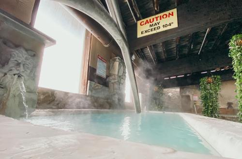 Indoor hot spring with steam rising, stone walls, and a caution sign about high temperatures.