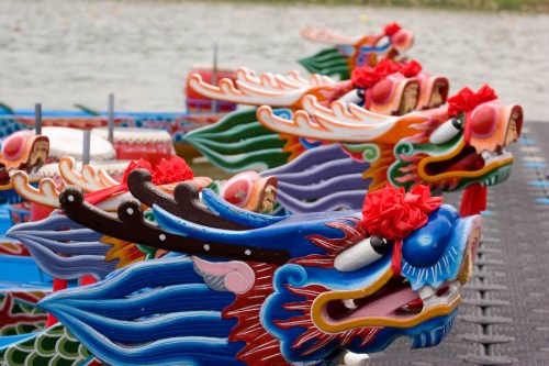 Colorful dragon heads of traditional boats lined up at a dock, ready for a dragon boat race on a calm water surface.