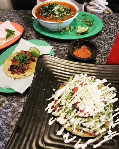 A colorful spread of Mexican dishes: a bowl of soup, a taco, and a tostada topped with lettuce, tomatoes, and cream.